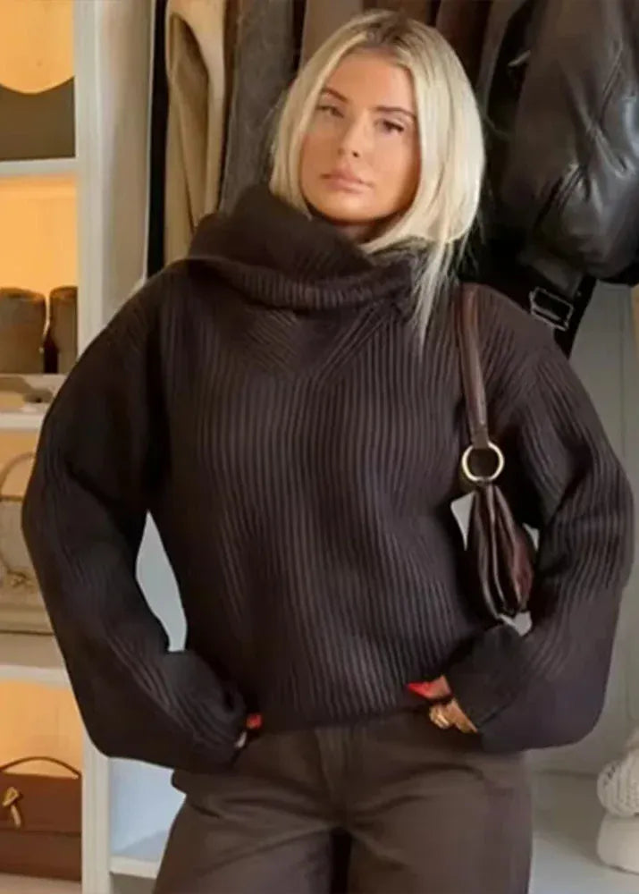 Woman wearing a dark ribbed sweater with a blurred indoor background