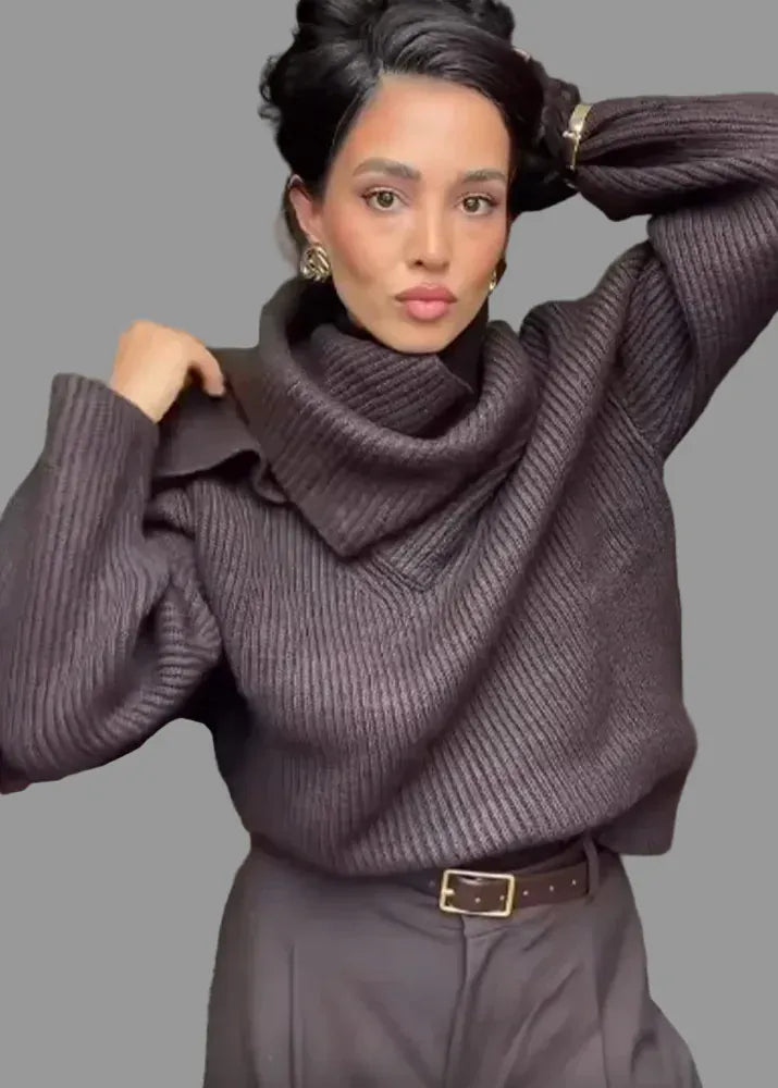 Woman wearing a dark purple sweater and pants, adjusting her hair indoors.