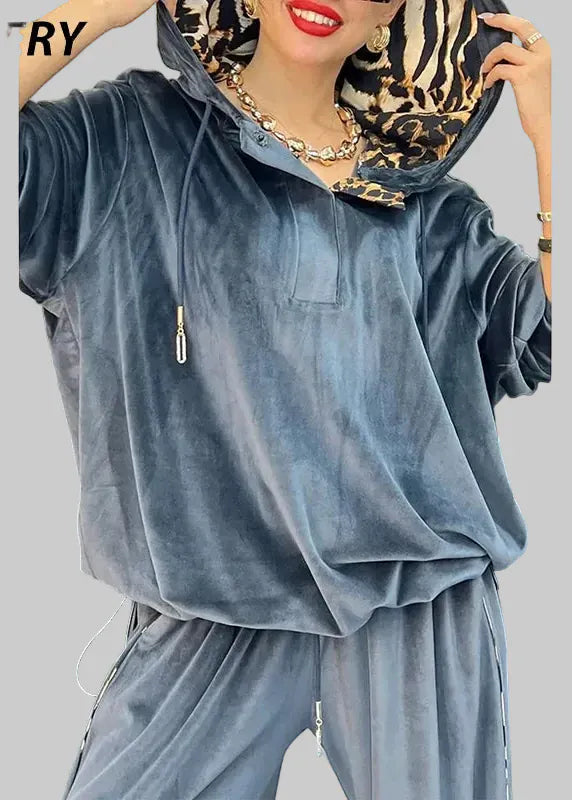 Person wearing a blue velour tracksuit with a leopard print headscarf, standing against a white background.