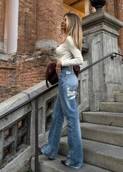 Woman in a white top and blue jeans standing on stone steps with a brick building in the background
