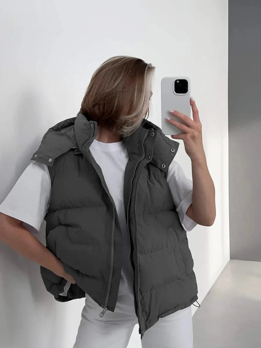 Person wearing a gray puffer vest holding a phone against a white background