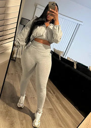 Person taking a mirror selfie wearing a gray outfit in a modern living room.