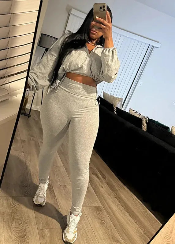 Person taking a mirror selfie wearing a gray outfit in a modern living room.