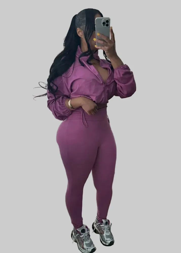Person taking a mirror selfie wearing a purple outfit in a room with a large window.