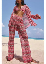 Person wearing a pink crochet outfit on a beach with blue sky and ocean.