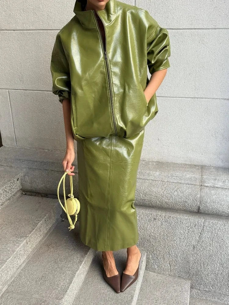 Person wearing a green leather outfit standing on steps with a gray wall background