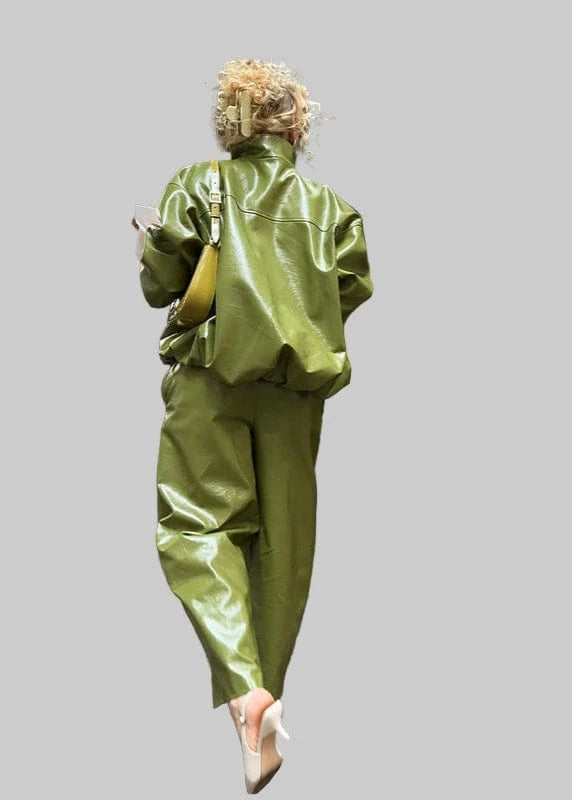 Person wearing a green outfit standing next to a green car under a wooden structure.