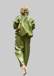 Person wearing a green outfit standing next to a green car under a wooden structure.