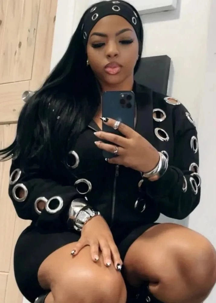 Woman taking a mirror selfie wearing a black outfit with circular cutouts, sitting on a chair.