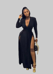 Woman in a black dress with a high slit standing in front of floral decorations and 'XSCAPE' branding.