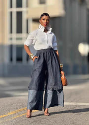 Woman in a white shirt and blue wide-leg pants standing on a street.