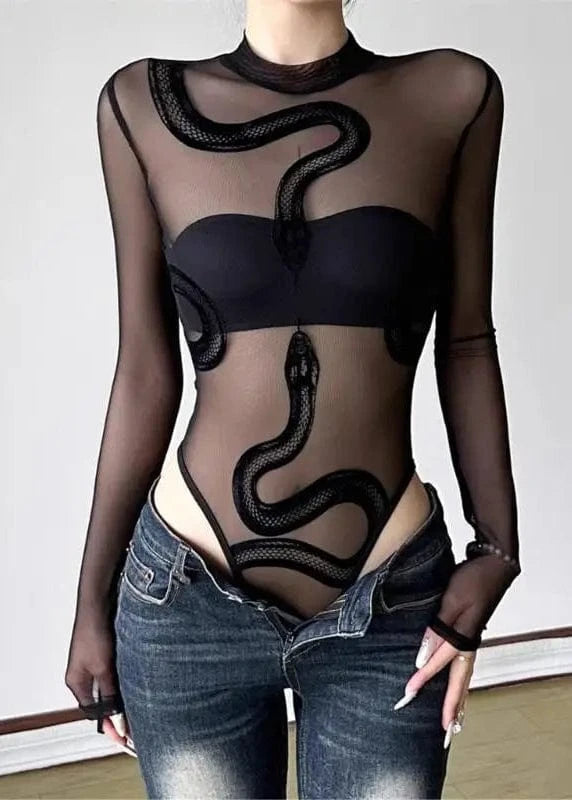 Person wearing a black sheer top with snake design and blue jeans on a plain background