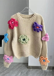 Beige sweater with colorful flower appliqués on a hanger against a gray wall.