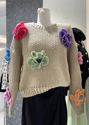 Beige sweater with colorful floral patches on a mannequin in a store setting.