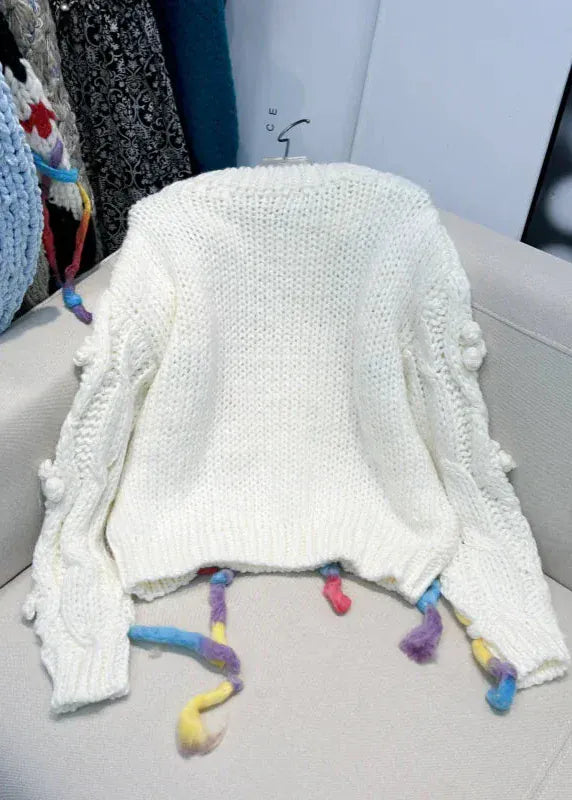 White knitted blanket with colorful tassels on a gray chair