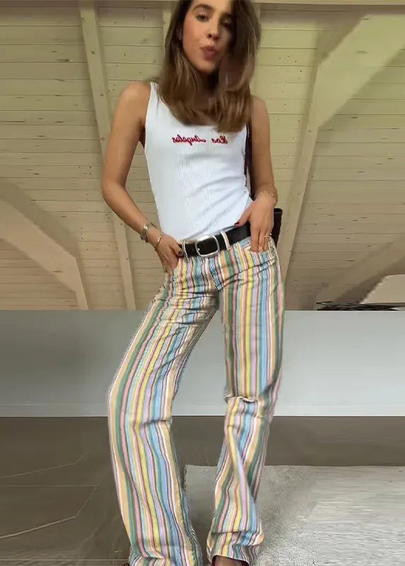 Woman wearing a white tank top with text and colorful striped pants indoors.
