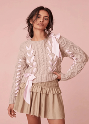 Woman wearing a beige sweater with pink ribbons and a matching skirt on a pink background