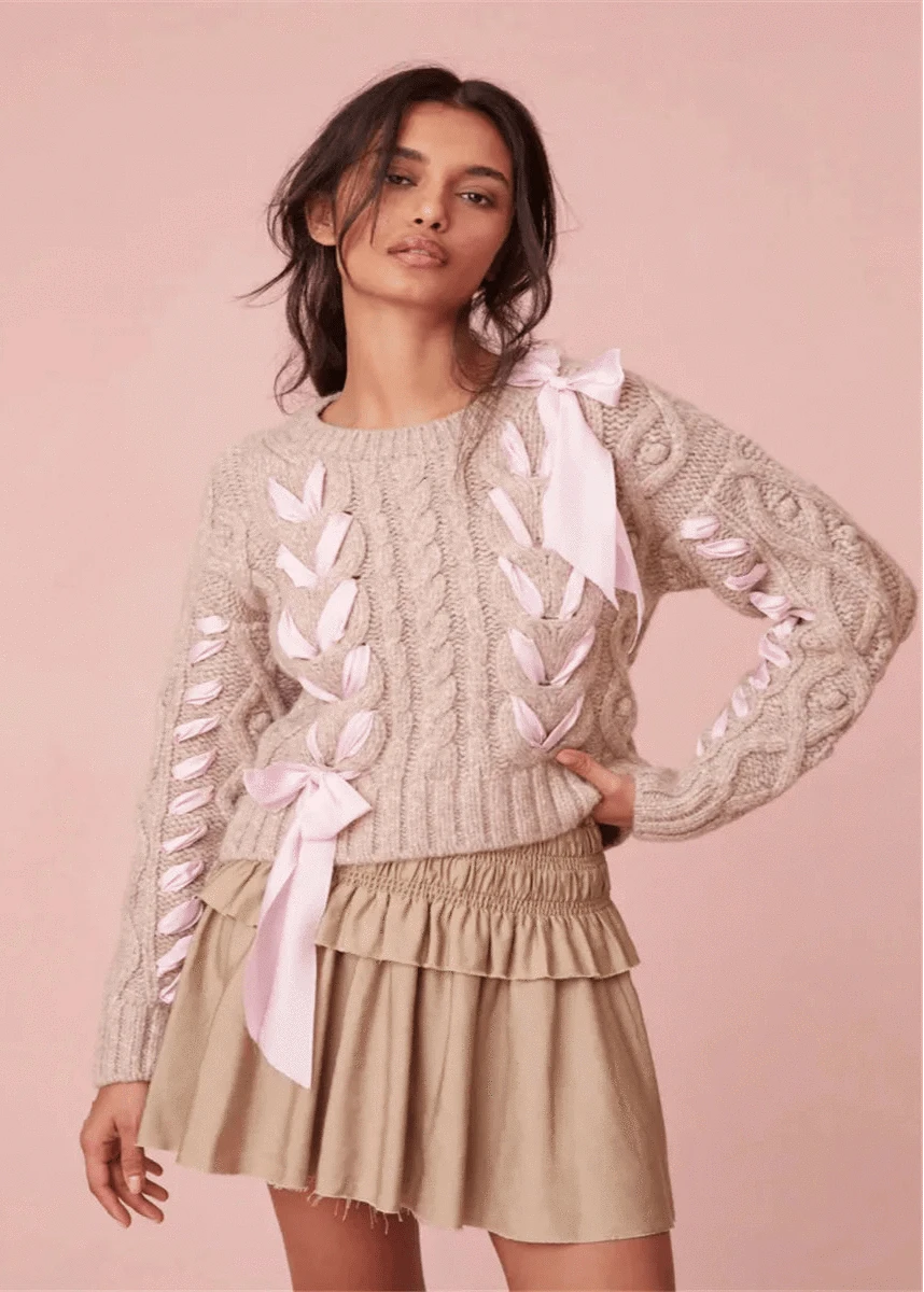 Woman wearing a beige sweater with pink ribbons and a matching skirt on a pink background