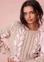 Woman wearing a beige sweater with pink feather-like embellishments against a pink background