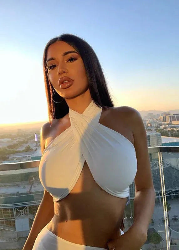 Woman in a white halter top standing on a rooftop with a cityscape in the background