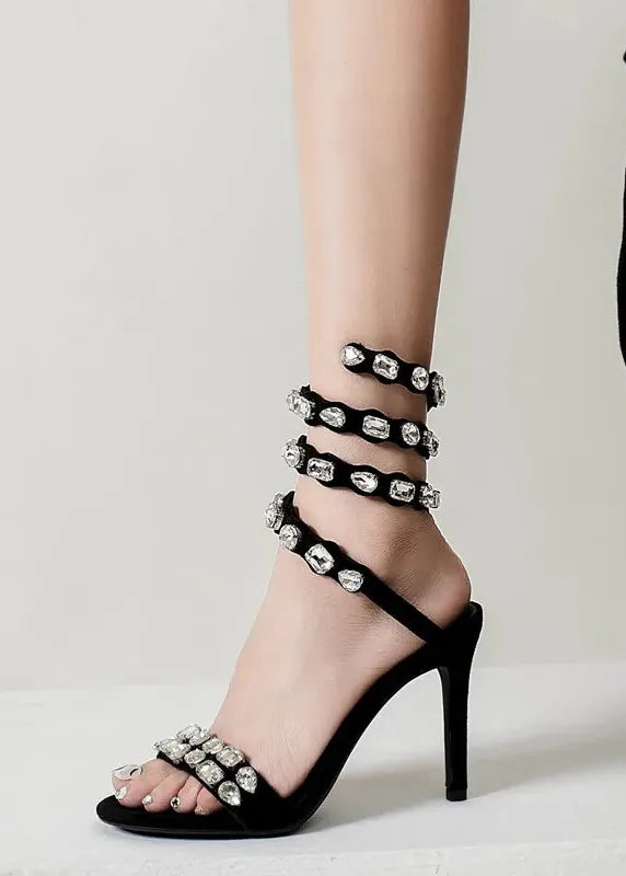 Black high-heeled sandals with decorative straps on a neutral background