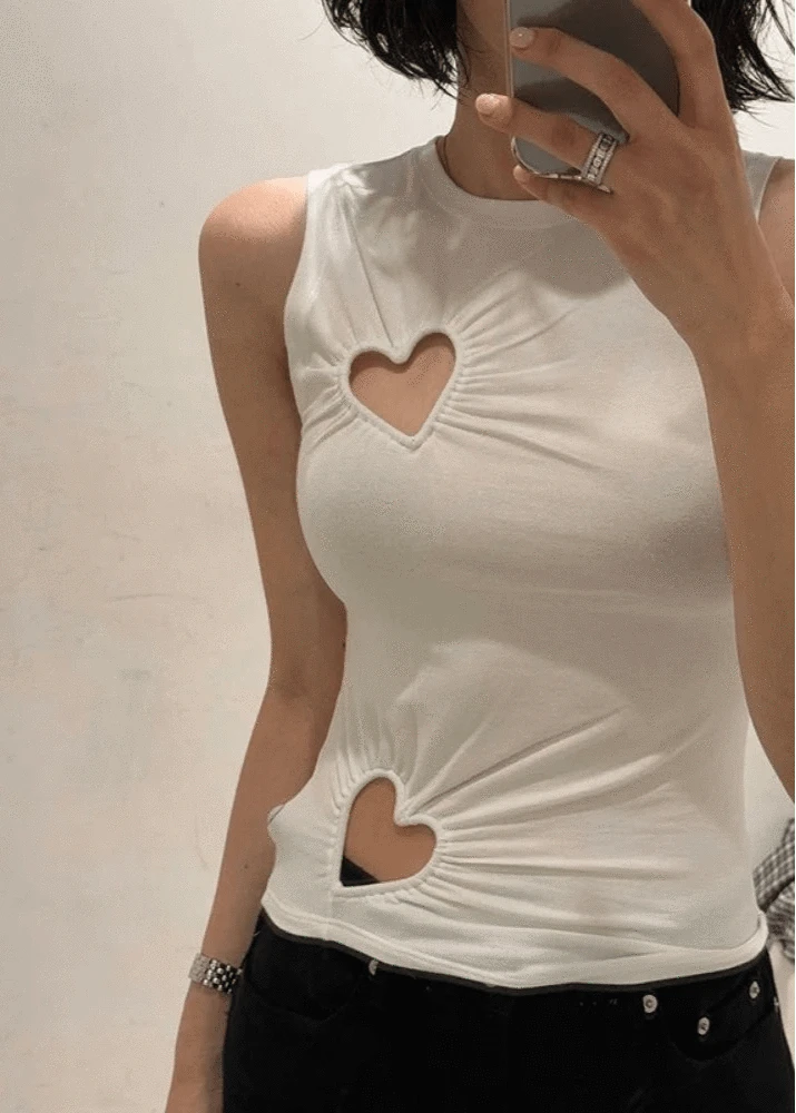 White sleeveless top with heart cutouts worn by a person against a plain background