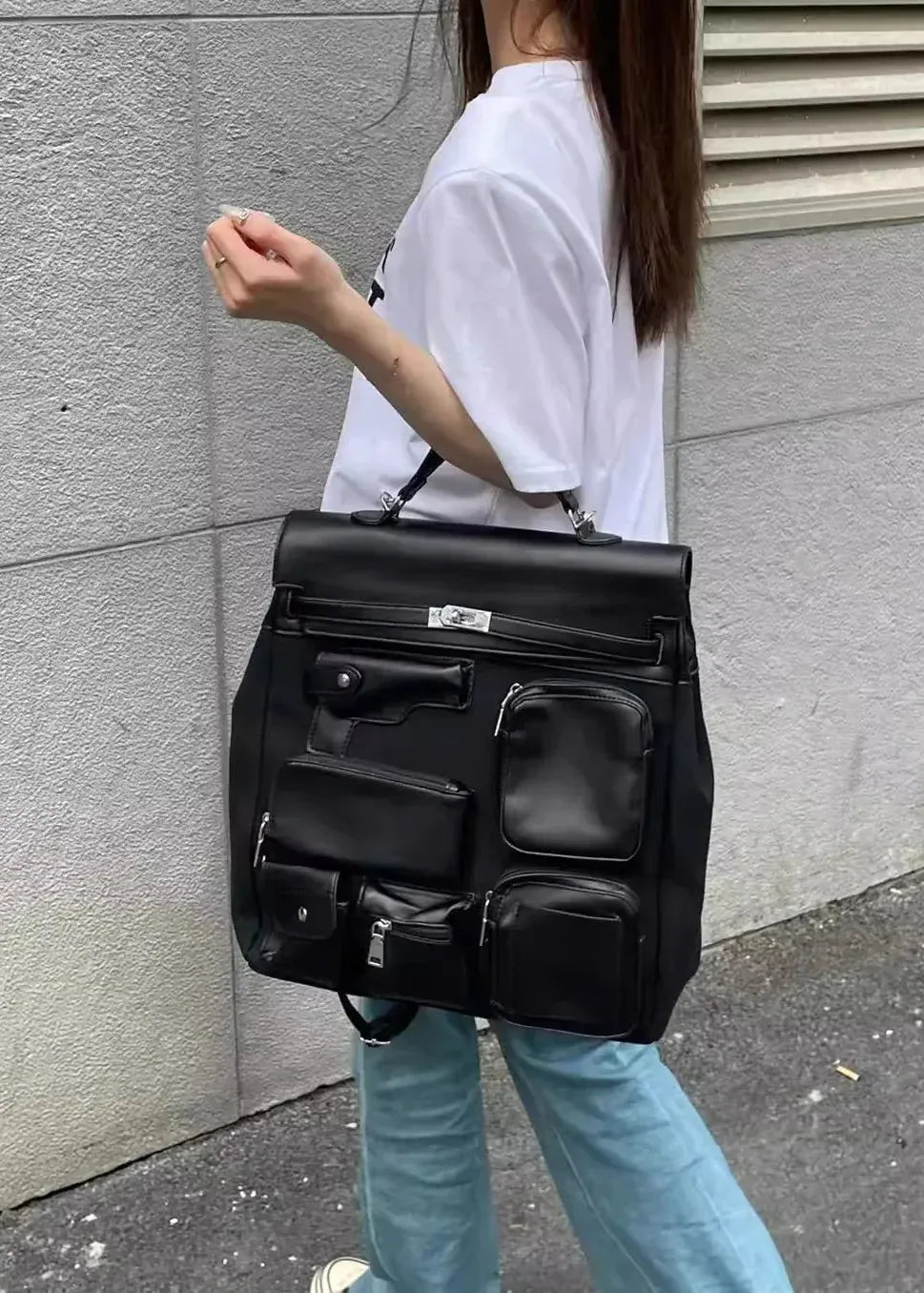 Person carrying a black backpack against a gray wall.