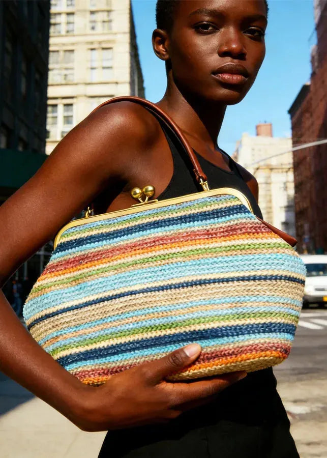 Woman holding a colorful striped handbag on a city street