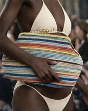 Model holding a colorful striped clutch bag on a runway