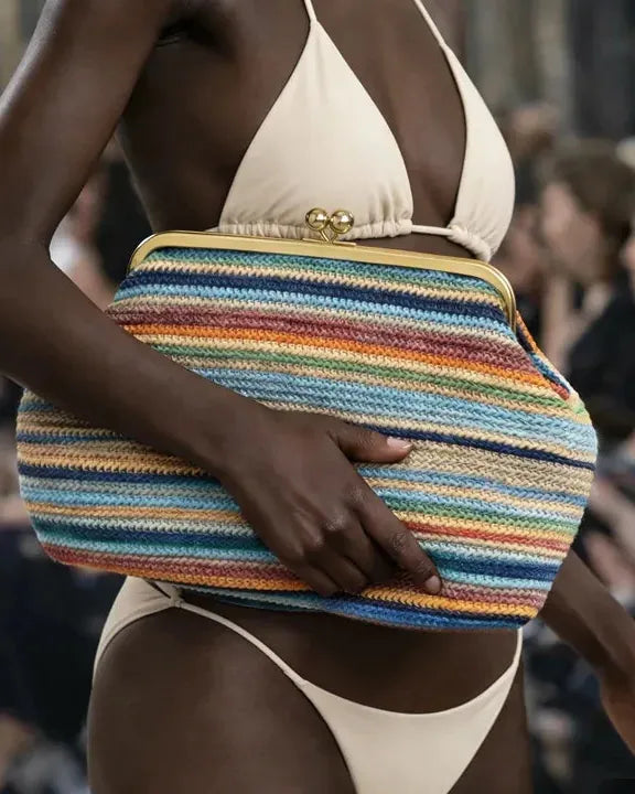 Model holding a colorful striped clutch bag on a runway