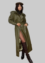 Woman in a long green coat and brown boots standing in an outdoor setting with columns and fallen leaves.