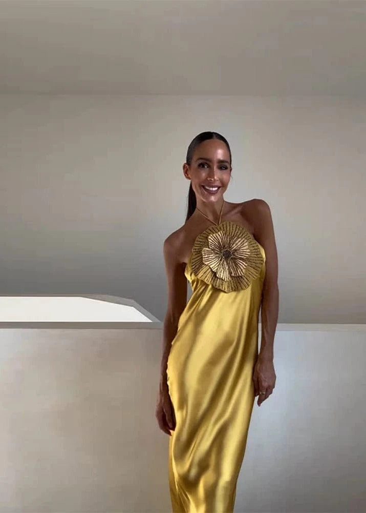 Woman wearing a gold evening gown with a sunburst design in a minimalistic setting.