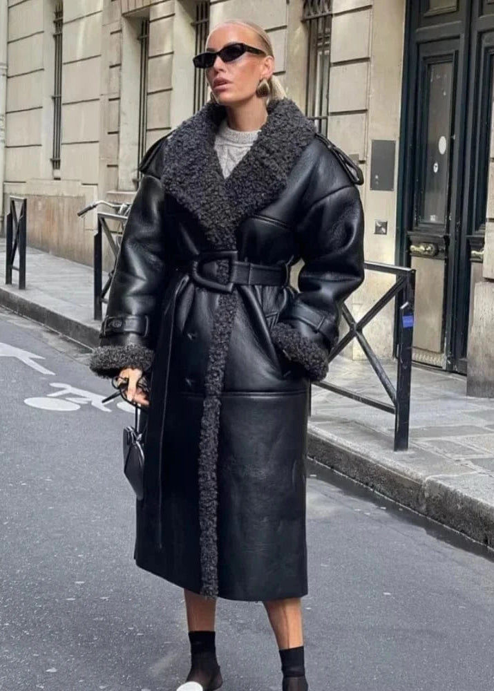 Person wearing a black leather coat with fur trim on a city street.