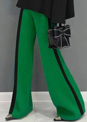 Green pants with black stripes and a black handbag with a bow on a gray background