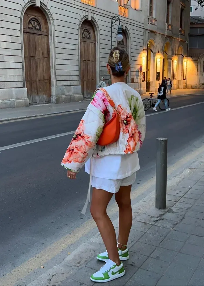 Person wearing a floral jacket and white outfit with green sneakers on a city street.