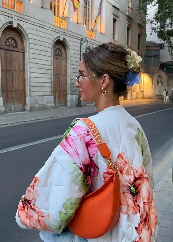 Woman in a floral kimono with an orange bag walking on a city street.