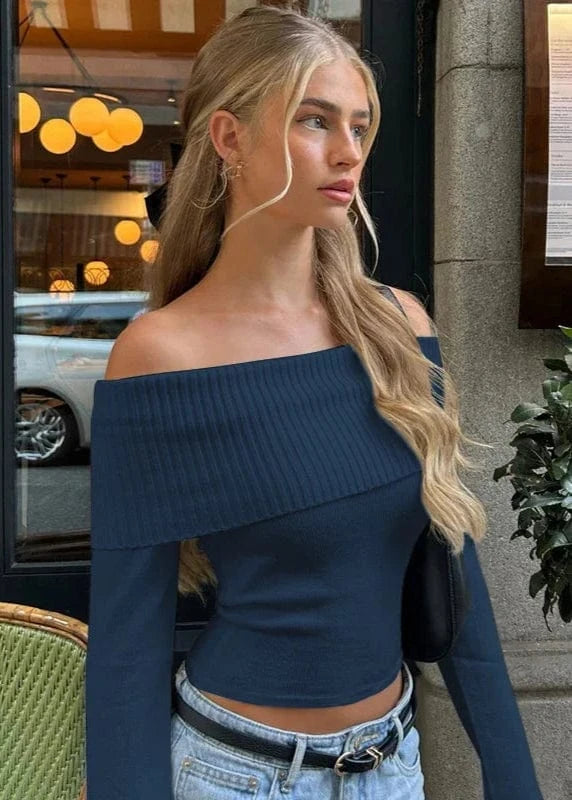 Woman wearing a blue off-shoulder top and jeans standing outdoors.