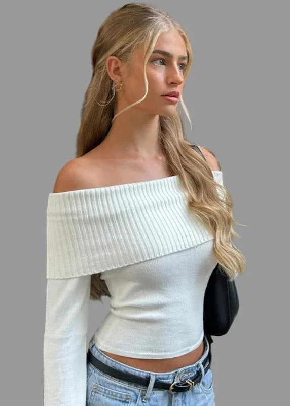 Woman wearing a white off-shoulder top and blue jeans standing outdoors.
