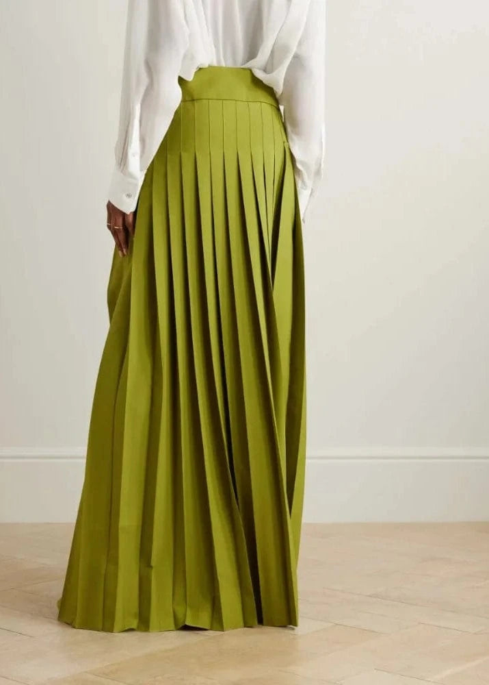 Person wearing a white blouse and green pleated skirt on a plain background
