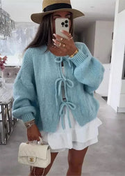 Person wearing a light blue cardigan with a white dress, holding a beige handbag indoors.