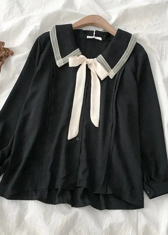 Black blouse with white lace collar and ribbon on a wooden hanger against a white fabric background