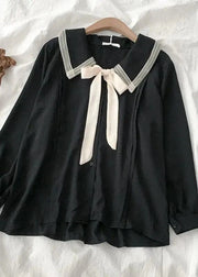 Black blouse with white lace collar and ribbon on a wooden hanger against a white fabric background