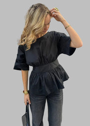 Woman in a black peplum top and gray pants on a city street.