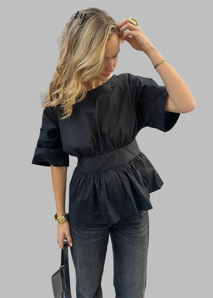 Woman in a black peplum top and gray pants on a city street.