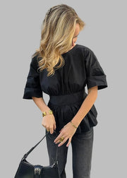 Woman in a black top and gray pants standing on a city street.
