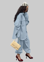 Woman in a light blue outfit with a beige handbag against a gray wall
