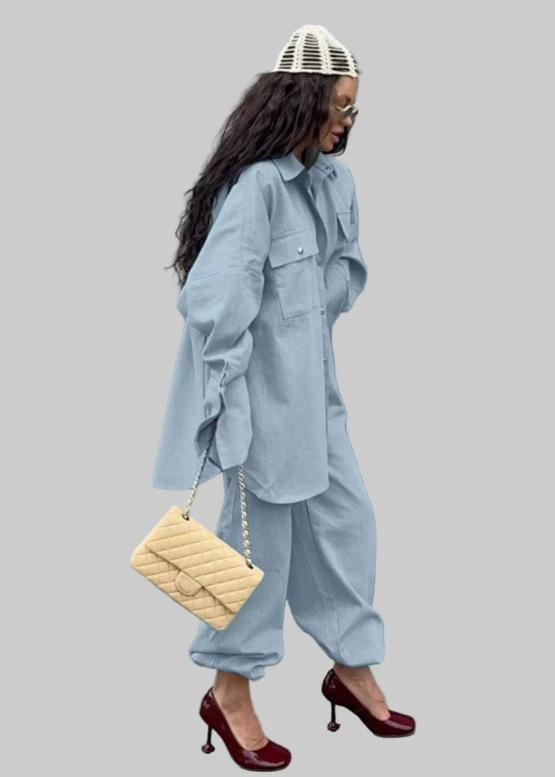 Woman in a light blue outfit with a beige handbag against a gray wall