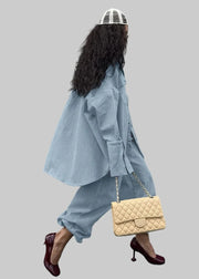 Person wearing a light blue outfit with a beige quilted handbag against a gray wall.