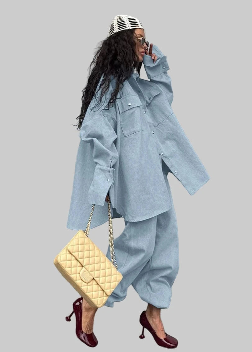 Person wearing a light blue outfit with a beige handbag against a gray wall.