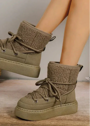 Brown fleece-lined boots on a wooden floor with a plant in the background